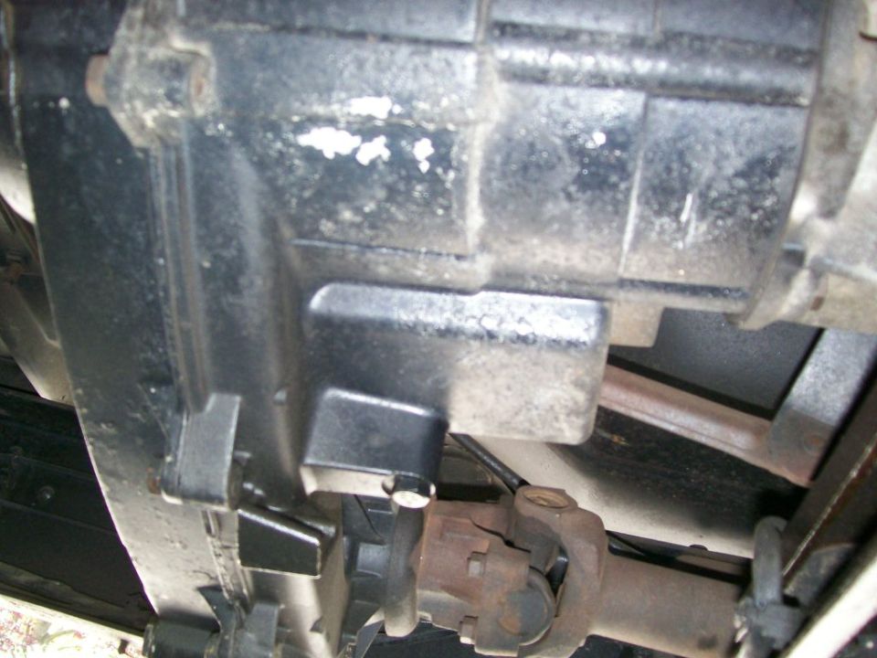 Grimy transfer case seen from underneath with a rusty driveshaft U-joint below
