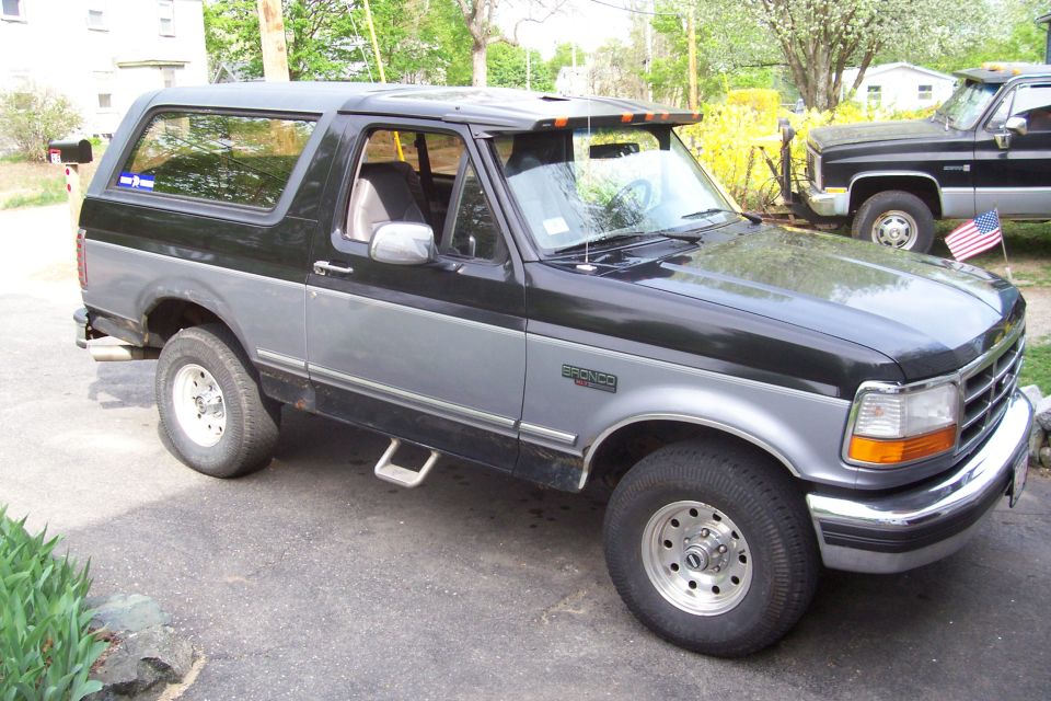 Two-tone black and gray Ford Bronco parked in a driveway, with another truck behind it