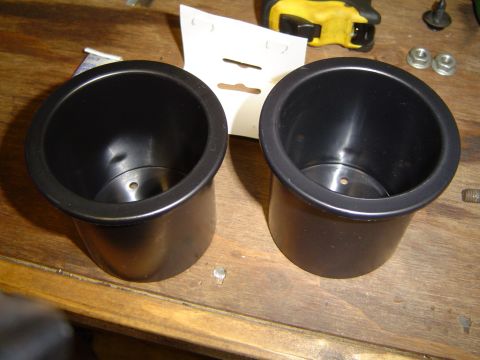 1989 Ford Bronco - Two black plastic cup holders are shown on a wooden surface, with some hardware and a measuring tape visible.