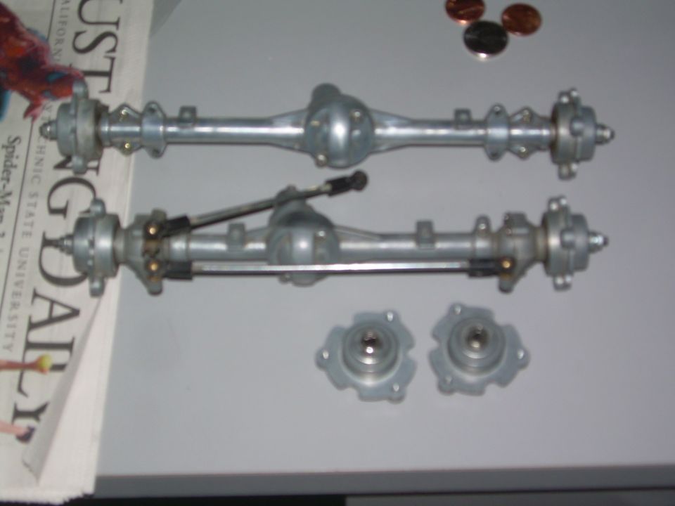 Two metal differential axles with brake components and two separate hubs on a gray surface