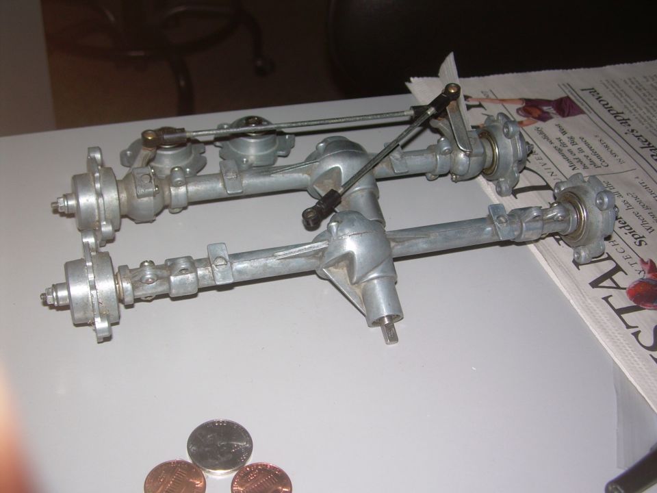 Two metal axles with suspension components and linkages, viewed from above on a table