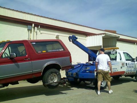 1995 Ford Bronco - Two-tone red-over-silver full-size Ford Bronco with a matching cap hoisted rear-first onto a blue wheel-lift tow truck lettered ALLIED TOWI…