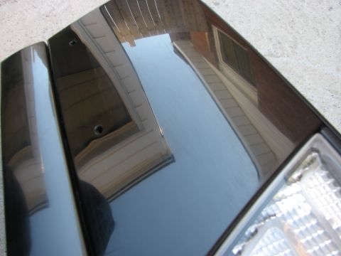 2003 Ford Crown Victoria - A dark colored car hood and fender are shown, reflecting a house and fence. The headlight is partially visible.