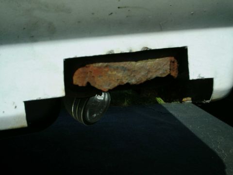 1988 Ford Bronco - A close-up view of a rusted section on a white vehicle, revealing a circular light underneath.