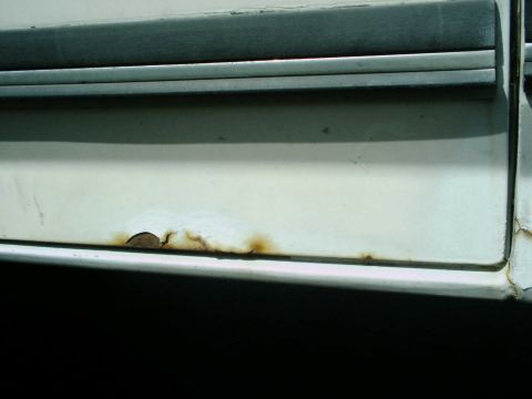 1988 Ford Bronco - Rust is visible on the lower portion of a white vehicle door, below a dark trim piece.