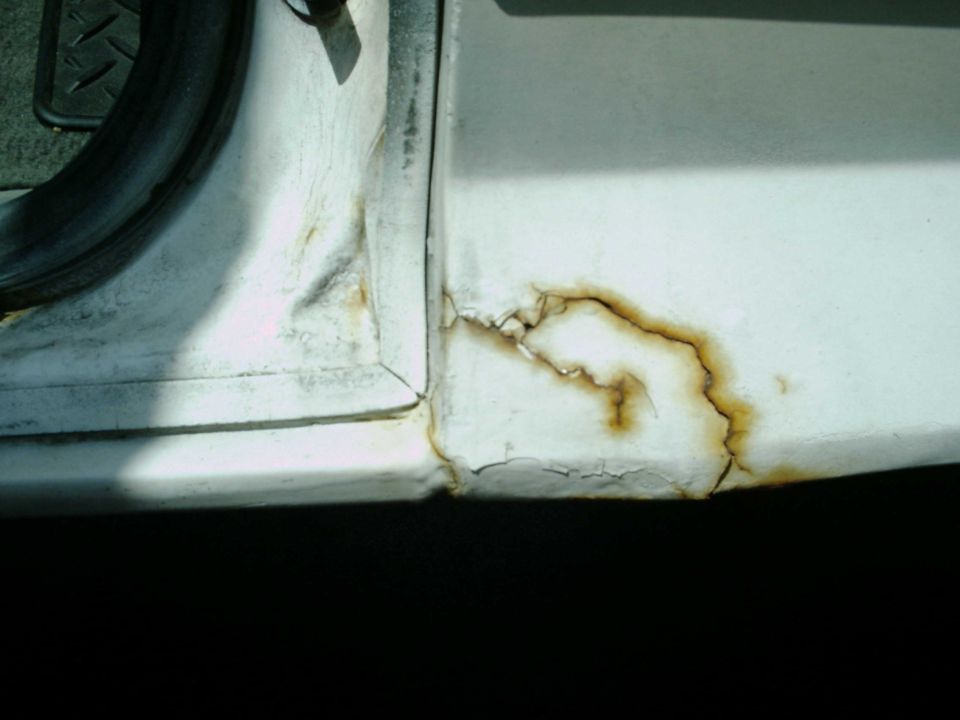 Rust damage and peeling paint on a white vehicle's door frame. Supermotors.net logo visible