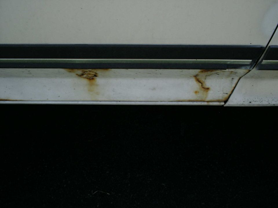 White vehicle's lower body trim shows rust spots and damage