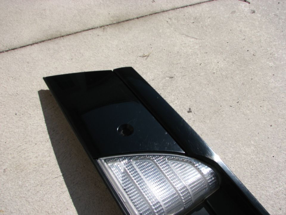Black car part with clear textured lens, possibly a tail light or marker light, on concrete