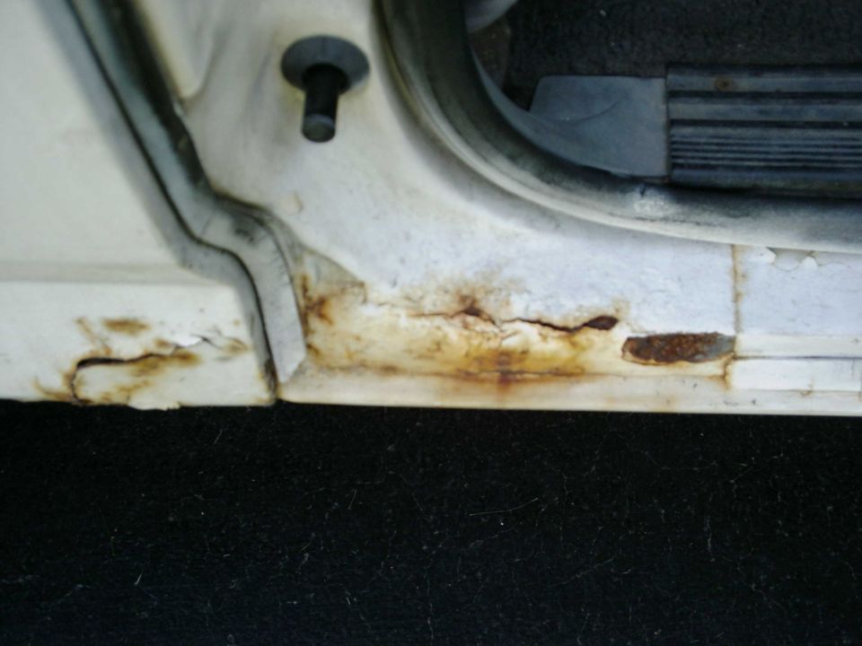 Close-up of a white vehicle's door sill showing significant rust damage