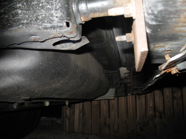 Vehicle underbody with fuel tank and rusted frame components, supported by wooden blocks