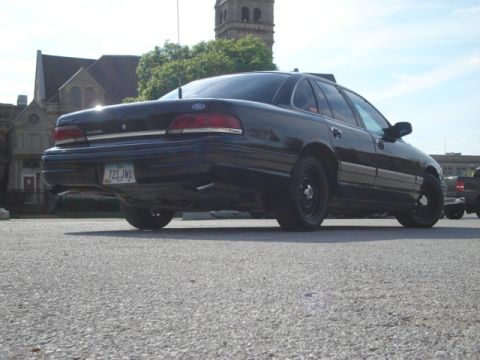 1992 Ford Crown Victoria - Rear view of a black 1992 Ford Crown Victoria parked outdoors with a building in the background.
