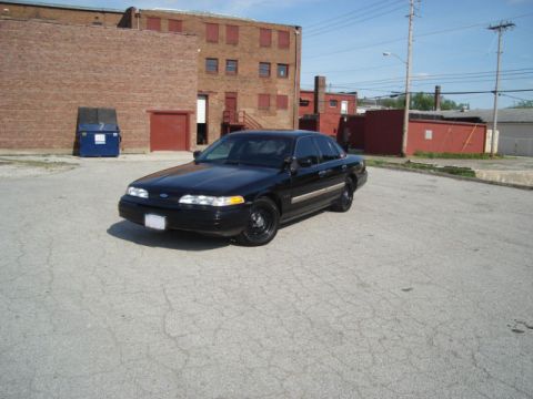 1992 Ford Crown Victoria - A black sedan is parked in an empty lot with a brick building in the background.