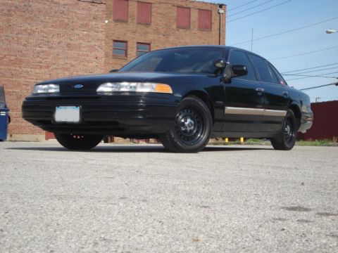 1992 Ford Crown Victoria - A black 1992 Ford Crown Victoria sedan is shown from the front 3/4 angle in front of a brick building.