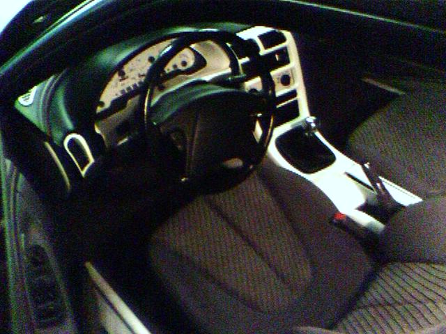 Car interior with dashboard, steering wheel, and gear shifter. Dark fabric seats