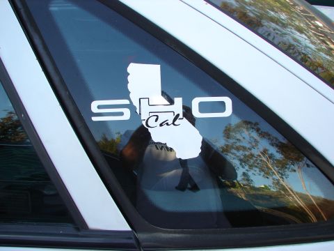 1992 Ford Taurus - A white sticker with 'SHO Cal' and a California outline is affixed to the rear window of a white vehicle.