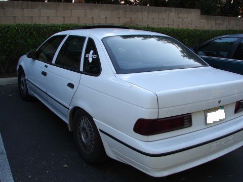 1992 Ford Taurus - A white 1992 Ford Taurus sedan is parked, showing its rear 3/4 view and a 'SHO' decal on the rear window.