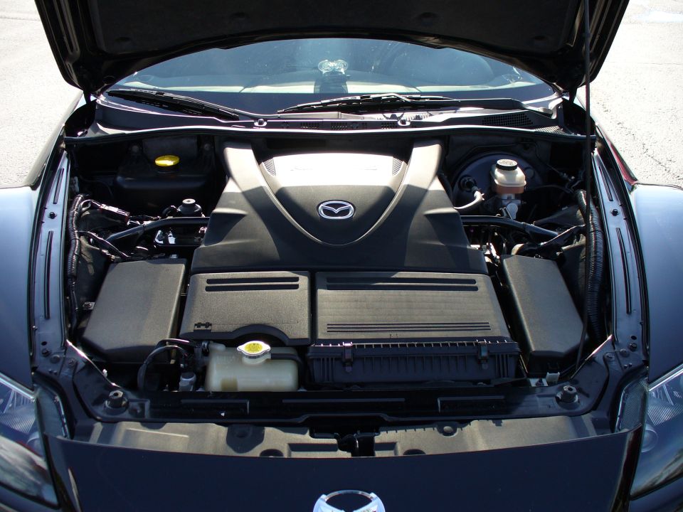 Mazda RX-8 engine bay with black plastic covers and a prominent Mazda logo