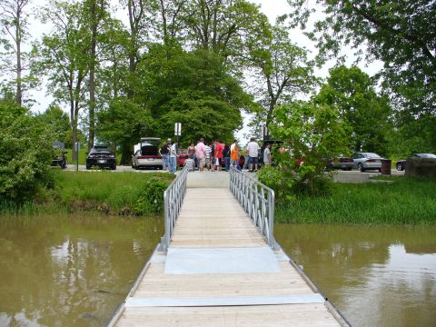 1991 Ford Probe - A group of people and several cars are gathered near a body of water, with a wooden walkway leading towards them.