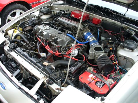 1991 Ford Probe - The engine bay of a car, a Ford badge and an aftermarket air intake system. Another vehicle is partially visible in the background.