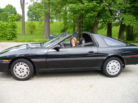 1991 Ford Probe - A black convertible sports car is parked outdoors with a woman in the driver's seat.