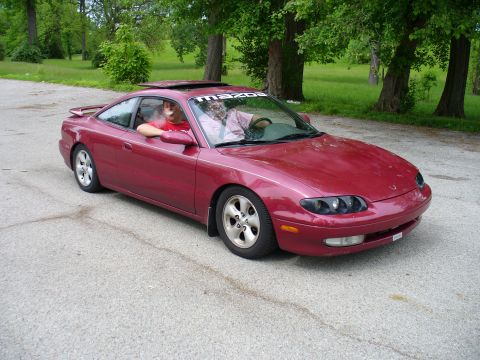 1991 Ford Probe - A red Mazda MX-6 is parked outside with two occupants visible through the windows.