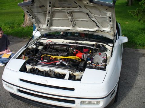1991 Ford Probe - The engine bay of a white 1991 Ford Probe is open, revealing the engine and aftermarket modifications.