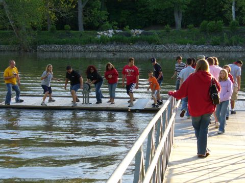 1991 Ford Probe - People gather on a floating dock by a river on a sunny day.