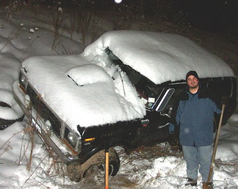 1978 Ford Bronco - A man stands with a shovel next to a 1978 Ford Bronco buried in snow.
