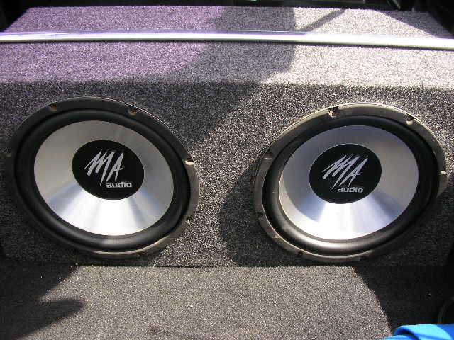 Dual MA audio subwoofers in a carpeted enclosure inside a vehicle's trunk