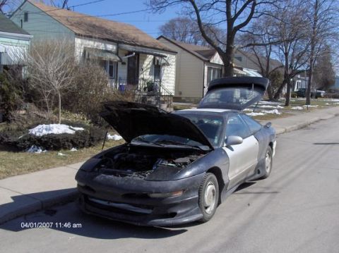 1993 Ford Probe - A 1993 Ford Probe sits on a residential street with its hood and trunk open, revealing the engine and cargo area.