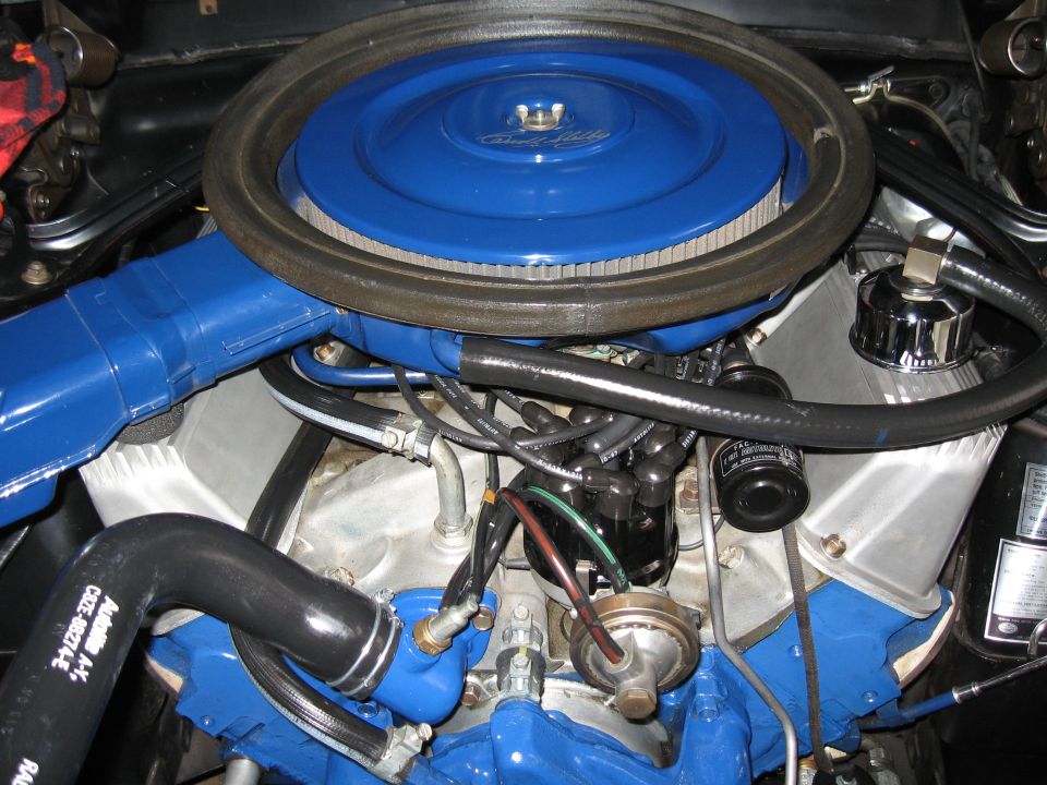 Close-up of a blue engine with a round air filter and various hoses and wires