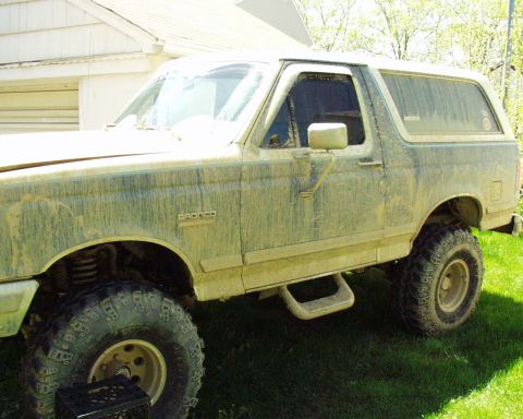 1989 Ford Bronco - This 1989 Ford Bronco is covered in mud, obscuring much of its original paintwork. The 'Bronco' badge is still visible on the fender.