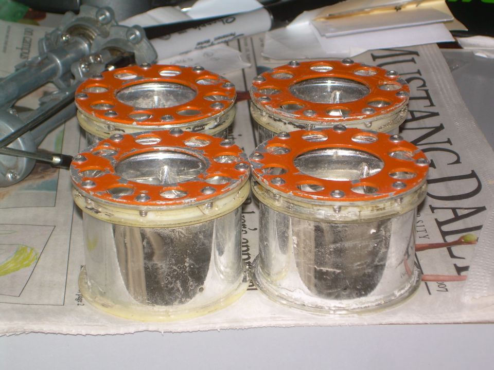 four cylindrical parts with orange flanges and screws, sitting on newspaper