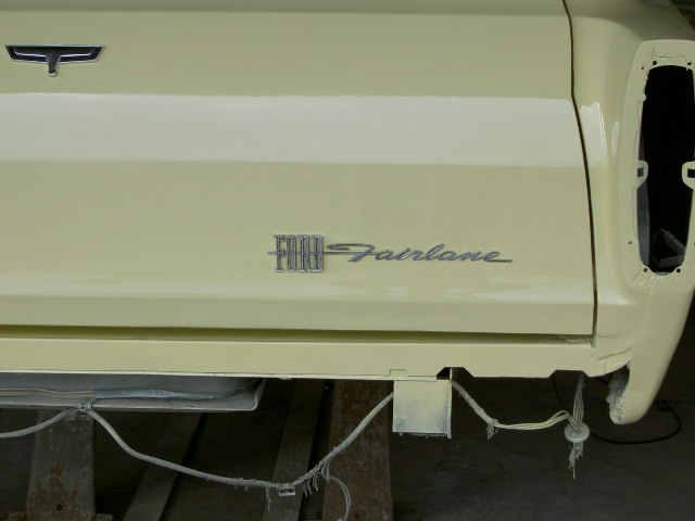 Side panel of a car with a Ford emblem and 'Fairlane' script. Tail light area is open