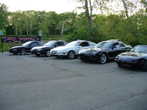 1991 Ford Probe - A group of Mazda sports cars are lined up in a parking lot with trees in the background.