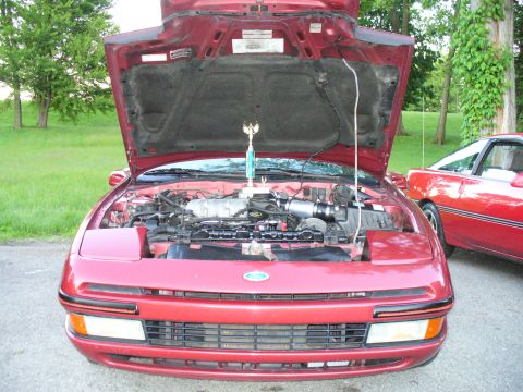 1991 Ford Probe - A red 1991 Ford Probe is displayed with its hood open, revealing the engine and a trophy, with another similar vehicle nearby.