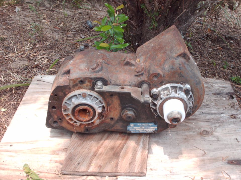 Rusty New Process Gear transfer case with ID tag sitting on plywood outdoors