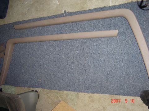 1993 Ford Bronco - Two tan interior trim pieces are shown laid out on a gray carpeted surface.