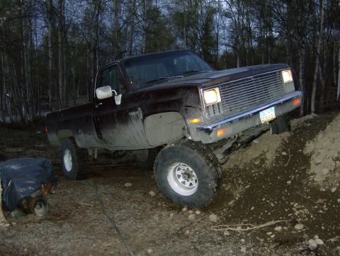 1982 Chevrolet C/K Pickup - A pickup truck navigates a dirt incline, with a spare engine nearby.