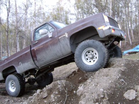 1982 Chevrolet C/K Pickup - This lifted pickup truck is navigating a challenging off-road course with steep inclines and loose dirt.