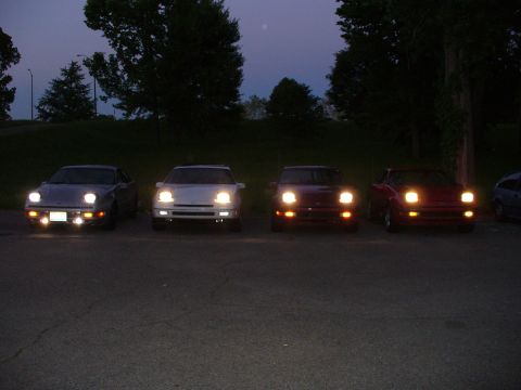1991 Ford Probe - Several cars are parked in a lot as the sky darkens, their headlights illuminating the scene.