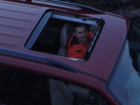 1974 Ford Bronco - A person leans out of the sunroof of a red vehicle.