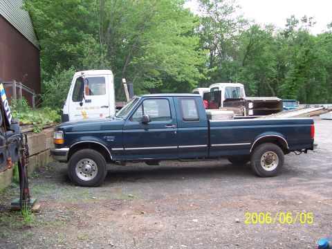 1990 Ford Bronco - A dark green Ford F-250 pickup truck is parked next to a white utility truck.