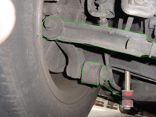 Close-up of a car's rear suspension with a tire on the left, showing control arms and bushings