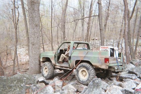 1969 Ford Bronco - A camouflaged pickup truck navigates a challenging rocky obstacle course in a wooded area.