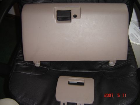 1993 Ford Bronco - A tan glove box door and its latch are shown, resting on a black leather surface.