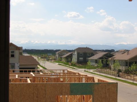 1995 Ford Bronco - View from a construction site shows framing for a new house, a suburban street, and distant snow-capped mountains under a partly cloudy sky.