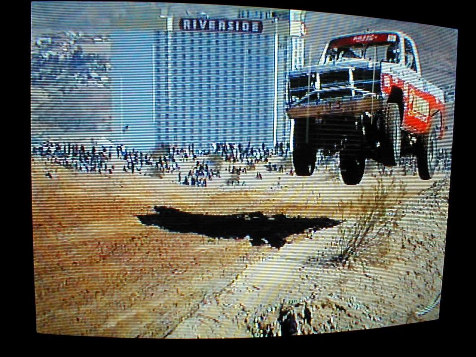 Off-road race truck mid-air jump, Riverside hotel in background