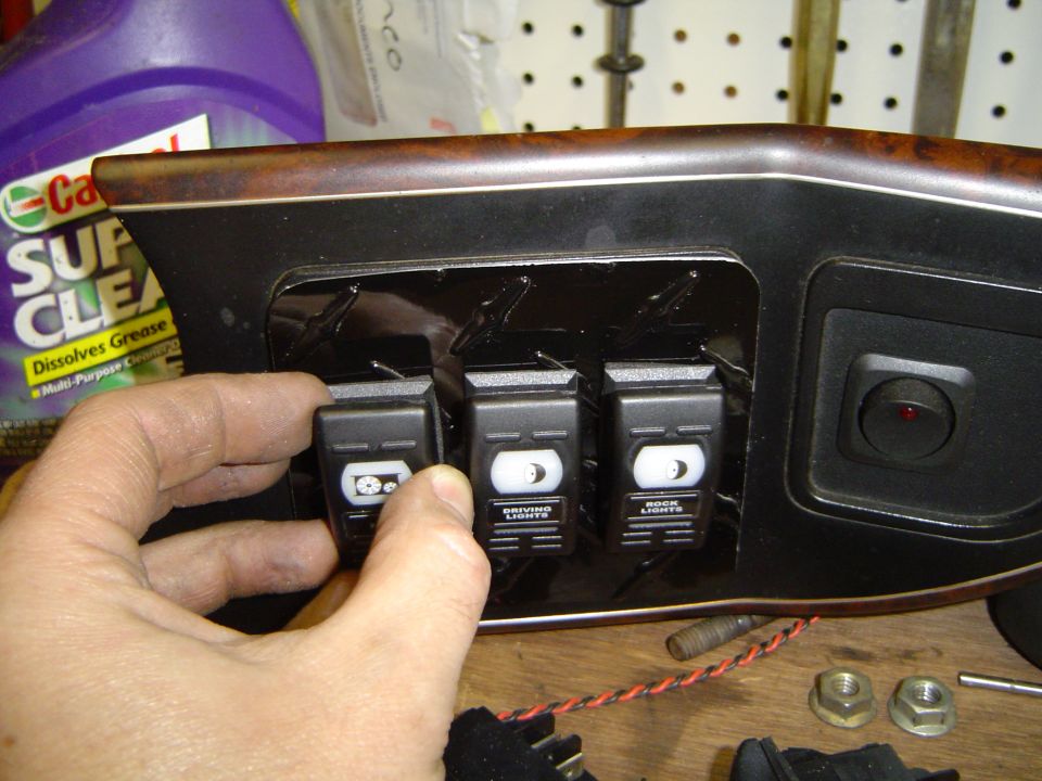 Hand installing three labeled rocker switches into a woodgrain switch panel