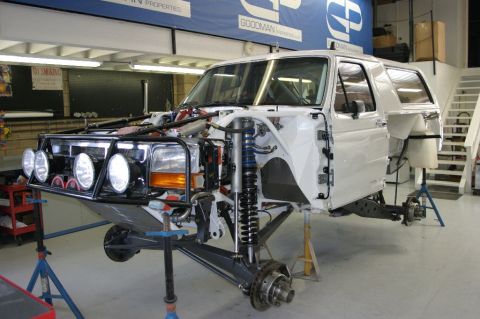 1996 Ford Bronco - A white Ford Bronco body shell mounted on jack stands during a prerunner build, with the front end stripped to reveal a tubular front bumpe…